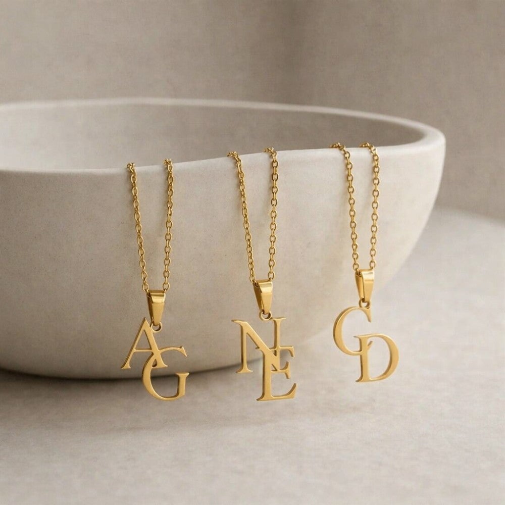 Three gold necklaces with letter pendants on a neutral background
